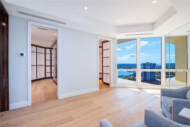 living room with a raised ceiling, floor to ceiling windows, a water view, and light wood-type flooring