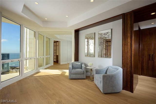 sitting room with a water view, light hardwood / wood-style floors, and a tray ceiling