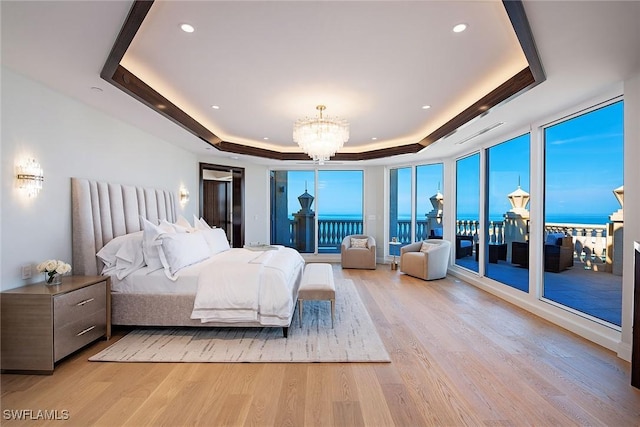 bedroom with a water view, a chandelier, access to outside, light wood-type flooring, and a raised ceiling