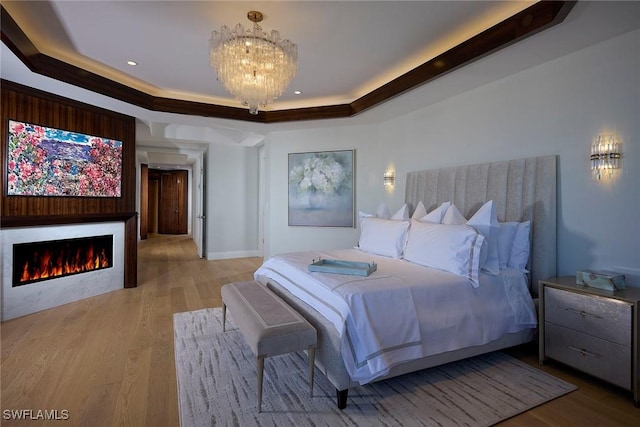 bedroom with a raised ceiling, an inviting chandelier, and light wood-type flooring