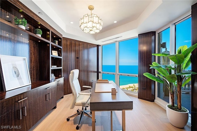 home office featuring light hardwood / wood-style flooring, an inviting chandelier, a water view, a wealth of natural light, and a raised ceiling