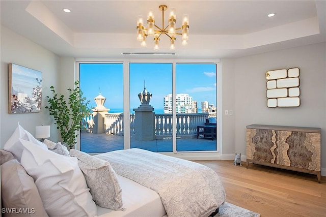 bedroom with hardwood / wood-style floors, a tray ceiling, access to outside, and a notable chandelier