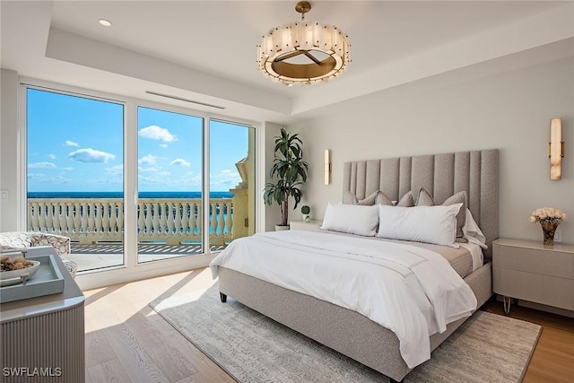 bedroom with a raised ceiling, wood-type flooring, a water view, and access to exterior