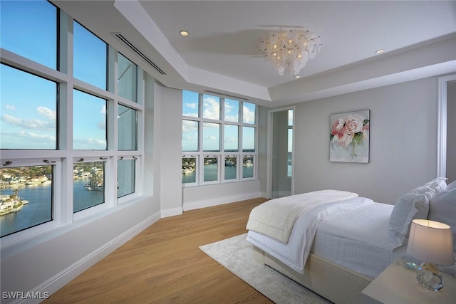 bedroom with multiple windows, a raised ceiling, an inviting chandelier, and light wood-type flooring