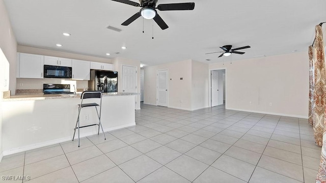 kitchen with light stone counters, a breakfast bar, ceiling fan, black appliances, and white cabinetry