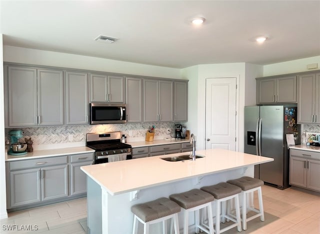 kitchen with gray cabinetry, sink, stainless steel appliances, a breakfast bar area, and a kitchen island with sink