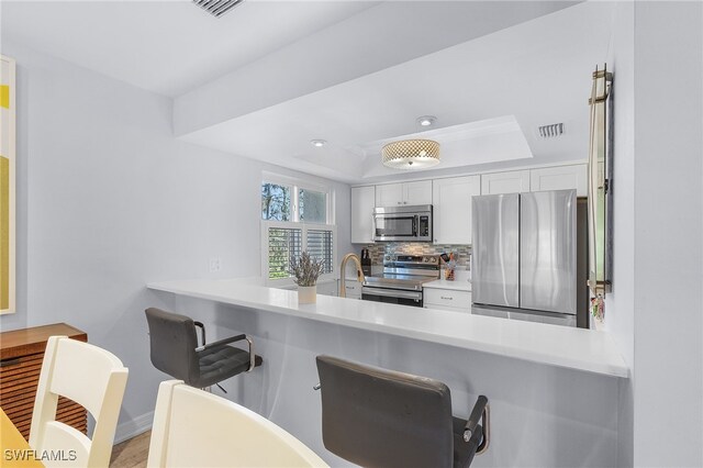 kitchen with decorative backsplash, light wood-type flooring, stainless steel appliances, a raised ceiling, and white cabinets