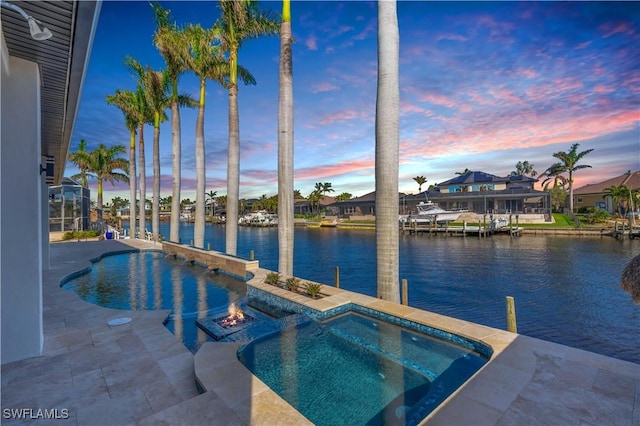 pool at dusk featuring a patio area, an outdoor fire pit, an in ground hot tub, and a water view