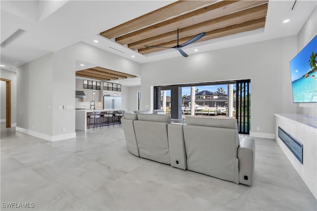 living room featuring a towering ceiling, a fireplace, sink, ceiling fan, and beam ceiling