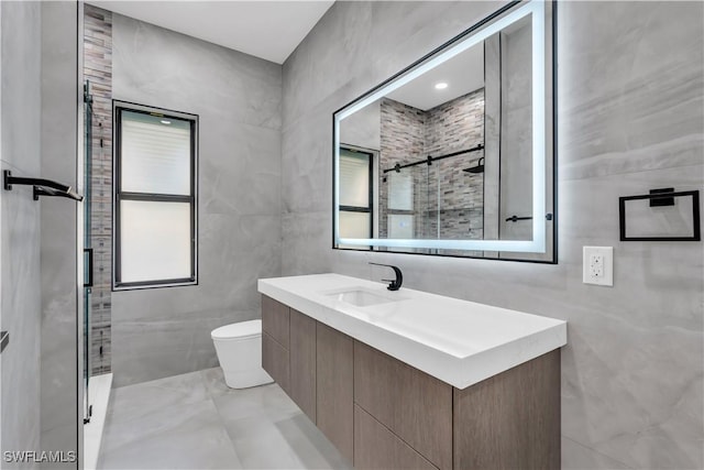 bathroom with tile walls, vanity, a shower with shower door, and toilet