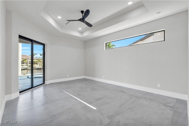 empty room with a water view, ceiling fan, a tray ceiling, and concrete floors