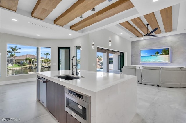 kitchen featuring sink, ceiling fan, a water view, a center island with sink, and beam ceiling