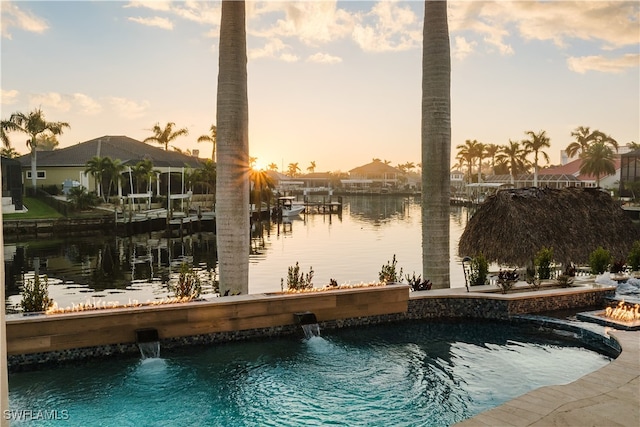 pool at dusk featuring pool water feature and a water view