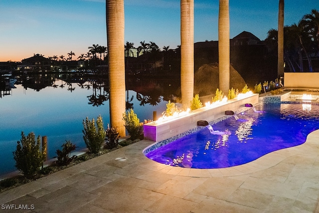 pool at dusk featuring a hot tub, a patio, pool water feature, and a water view