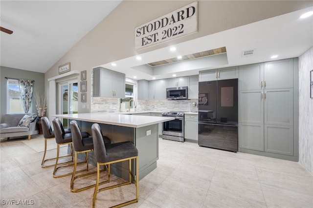 kitchen featuring a kitchen breakfast bar, stainless steel appliances, gray cabinets, and lofted ceiling