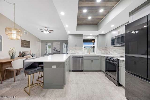 kitchen featuring gray cabinetry, black appliances, a kitchen breakfast bar, decorative backsplash, and kitchen peninsula