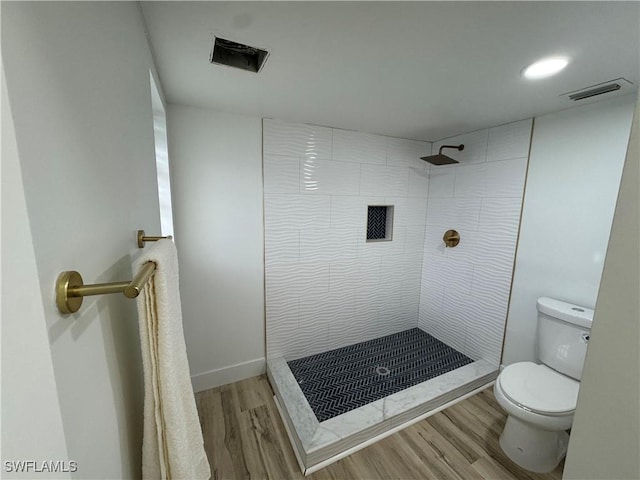 bathroom featuring a tile shower, toilet, and wood-type flooring