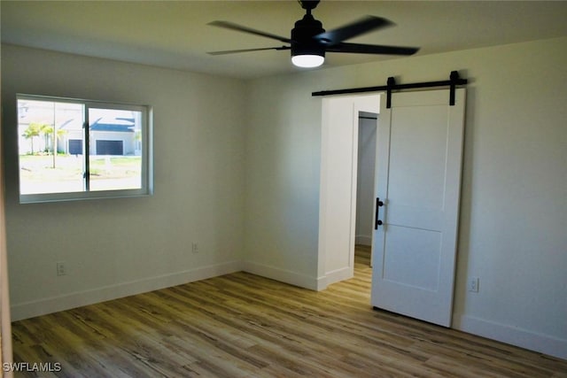 empty room featuring a barn door, ceiling fan, and hardwood / wood-style floors