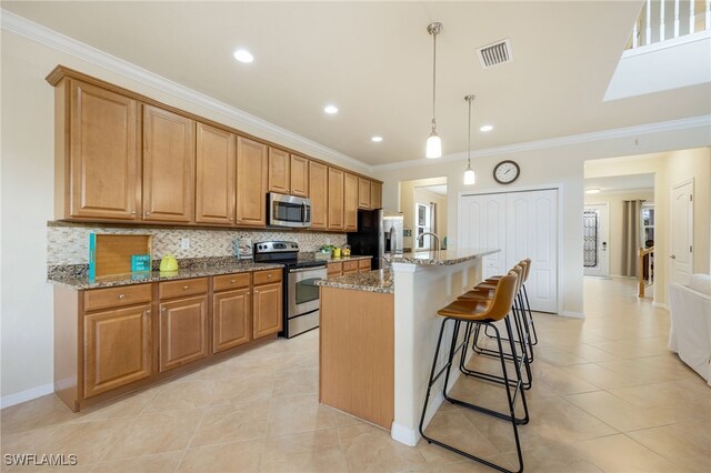 kitchen with hanging light fixtures, decorative backsplash, an island with sink, appliances with stainless steel finishes, and light stone counters