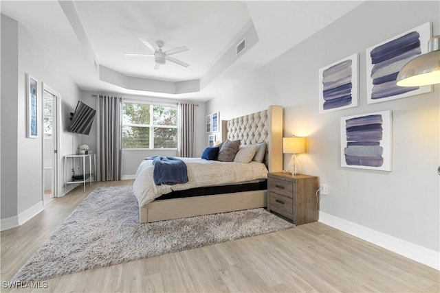 bedroom featuring ceiling fan, a tray ceiling, and light hardwood / wood-style floors