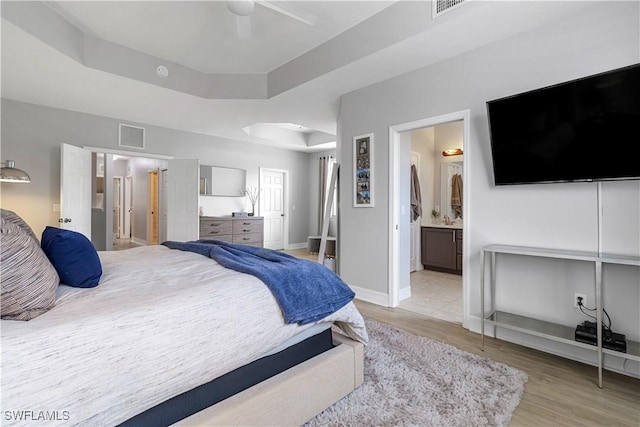 bedroom featuring connected bathroom, a raised ceiling, ceiling fan, and light wood-type flooring