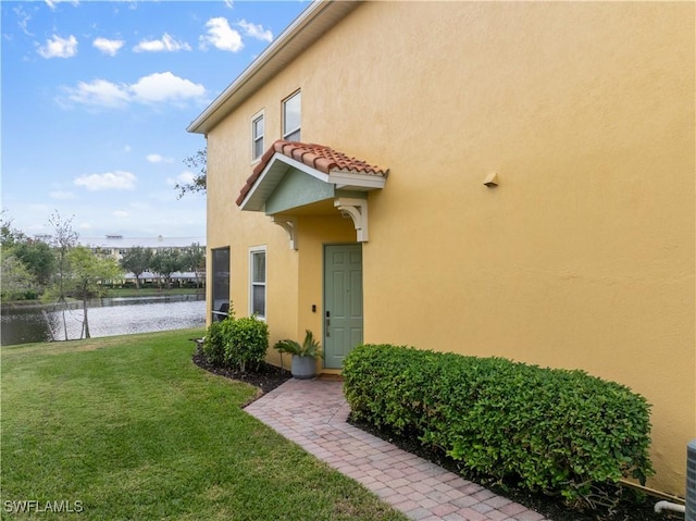 view of exterior entry with a water view and a yard