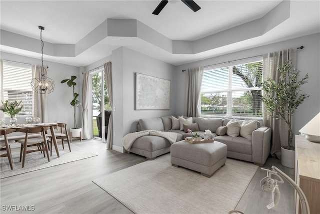 living room featuring a tray ceiling, ceiling fan with notable chandelier, and light hardwood / wood-style flooring