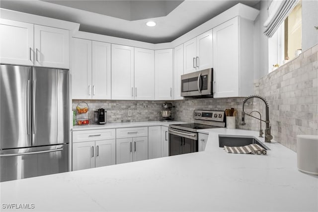 kitchen with sink, light stone counters, appliances with stainless steel finishes, decorative backsplash, and white cabinets