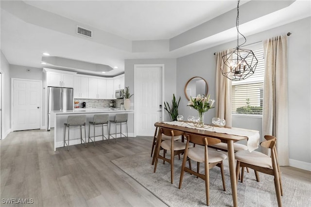 dining area featuring a raised ceiling, light wood-type flooring, and a notable chandelier