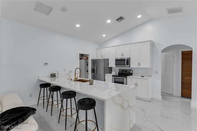 kitchen with kitchen peninsula, appliances with stainless steel finishes, vaulted ceiling, white cabinets, and a breakfast bar area