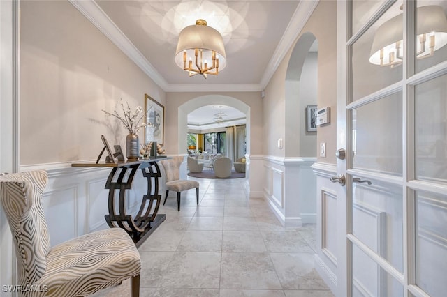 entryway with arched walkways, a wainscoted wall, an inviting chandelier, crown molding, and a decorative wall