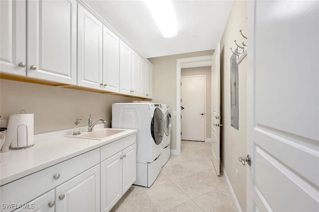 washroom featuring cabinet space, light tile patterned floors, baseboards, washing machine and clothes dryer, and a sink