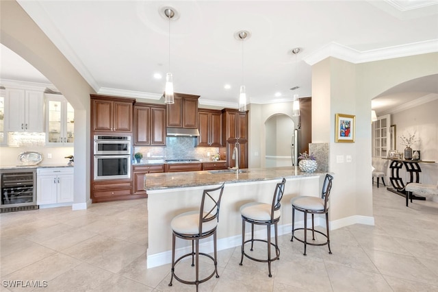 kitchen featuring stainless steel double oven, beverage cooler, a sink, light stone countertops, and cooktop