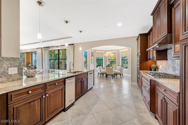 kitchen featuring arched walkways, light stone counters, stainless steel appliances, under cabinet range hood, and a sink