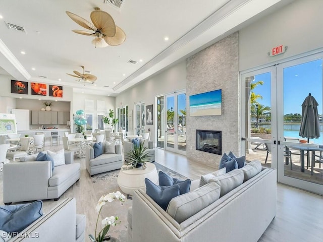 living room featuring a tray ceiling, a stone fireplace, french doors, and light hardwood / wood-style flooring