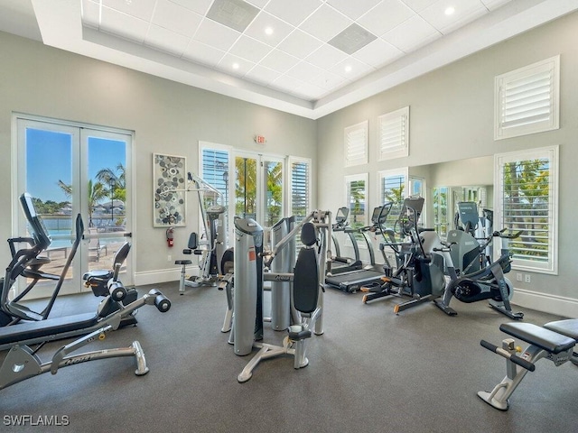 gym with a towering ceiling, a wealth of natural light, and a tray ceiling