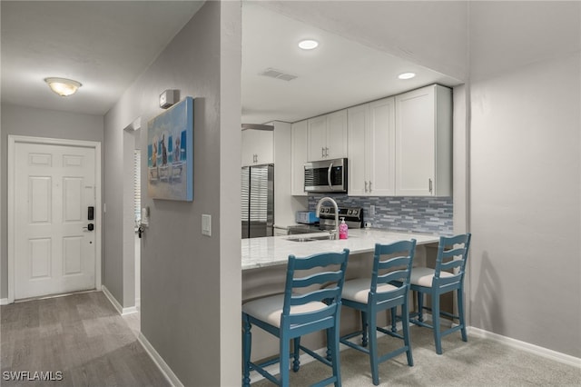 kitchen featuring white cabinets, appliances with stainless steel finishes, a breakfast bar, and backsplash