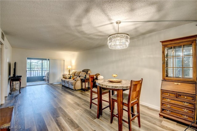 dining room with wood-type flooring, a textured ceiling, and a notable chandelier