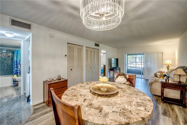 dining space featuring light wood-type flooring, a textured ceiling, and an inviting chandelier