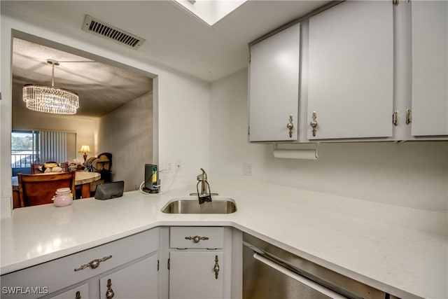 kitchen with white cabinets, sink, hanging light fixtures, stainless steel dishwasher, and a chandelier