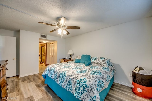 bedroom with ceiling fan, wood-type flooring, a textured ceiling, and ensuite bath