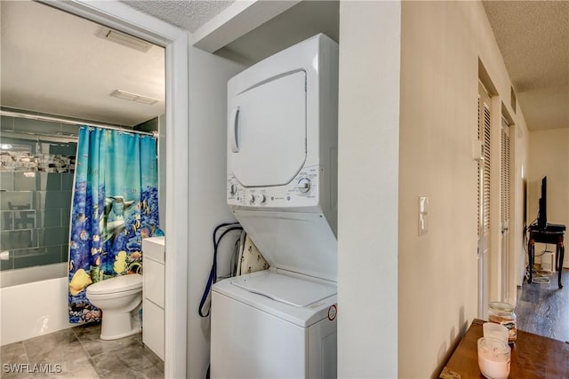 clothes washing area with tile patterned floors, a textured ceiling, and stacked washer and clothes dryer