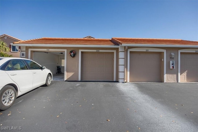 townhome / multi-family property featuring a tiled roof, community garages, and stucco siding