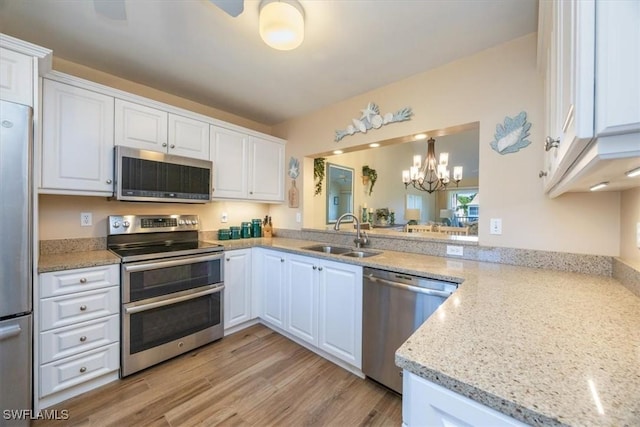 kitchen featuring light stone counters, stainless steel appliances, a sink, light wood-style floors, and white cabinets