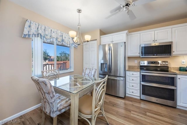 kitchen featuring light wood finished floors, stainless steel appliances, light countertops, white cabinets, and baseboards