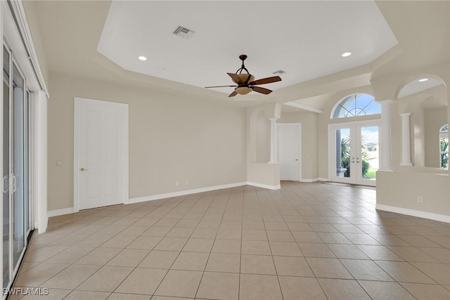 unfurnished living room with ceiling fan, light tile patterned floors, a raised ceiling, and french doors