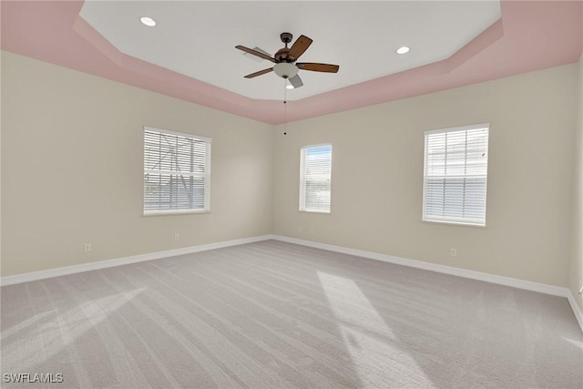 empty room with light carpet, ceiling fan, and a tray ceiling