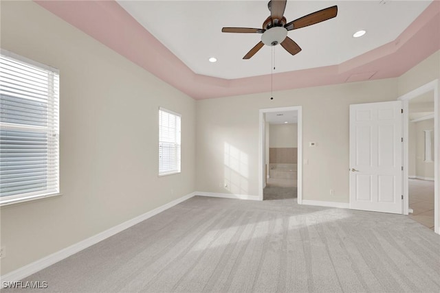 unfurnished bedroom with ceiling fan, connected bathroom, a raised ceiling, and light carpet