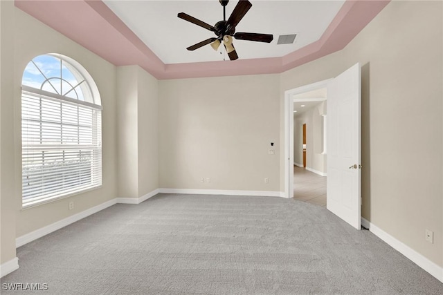 empty room featuring ceiling fan, light colored carpet, and a tray ceiling