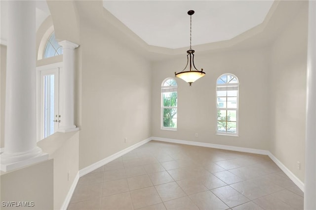 empty room featuring a raised ceiling, light tile patterned floors, and ornate columns